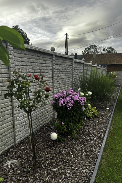 Ein gepflegter Garten mit bunten Blumen und einem stabilen Betonzaun im Hintergrund, der eine harmonische Trennung zwischen dem Garten und dem Nachbargrundstück bietet."